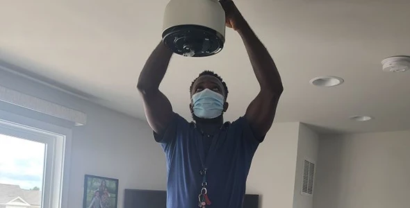 Electrician in a mask holding a light fixture for residential electrical services.