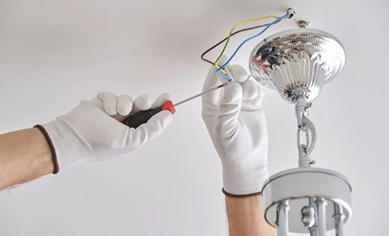 Electrician installing modern chandelier, highlighting interior light fixture installation and upgrade services in Arlington, VA.